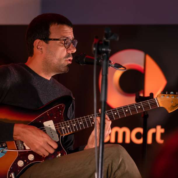 Miguel Araújo sentado numa cadeira a cantar e a tocar guitarra no palco do concessionário smart 
